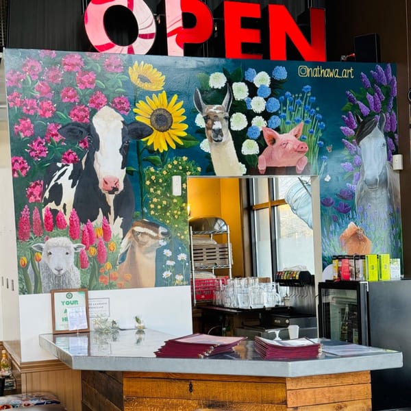 A colorful mural of farm animals and flowers behind a counter with menus at The Wayward Cafe.