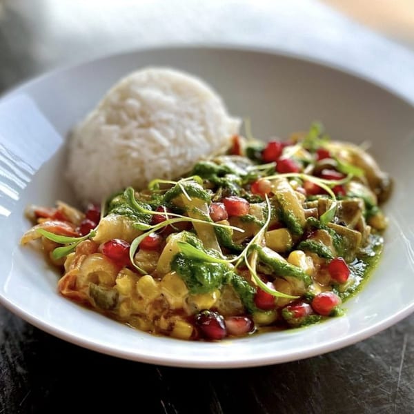 A Wayward Cafe dish with rice, a colorful vegetable medley, green sauce, and pomegranate seeds.
