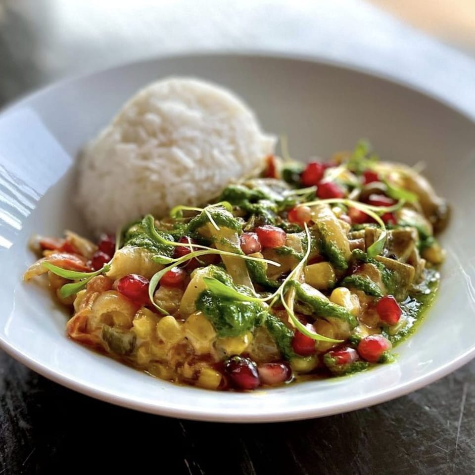 A Wayward Cafe dish with rice, a colorful vegetable medley, green sauce, and pomegranate seeds.