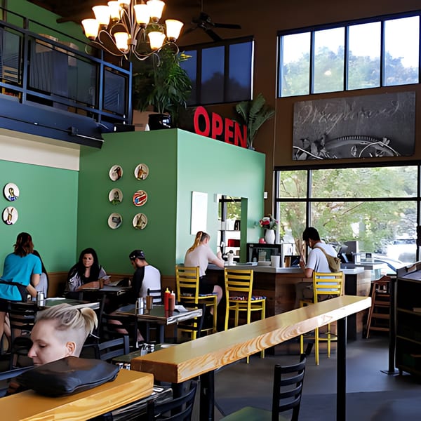 The Wayward Cafe's interior, with customers dining at tables and a counter, featuring green walls and large windows.