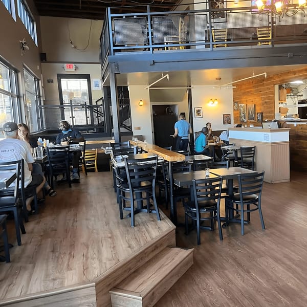 The Wayward Cafe's spacious dining area features a mezzanine, wooden floors, and patrons enjoying meals.