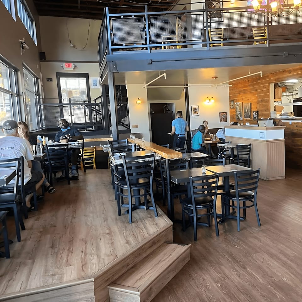The Wayward Cafe's spacious dining area features a mezzanine, wooden floors, and patrons enjoying meals.