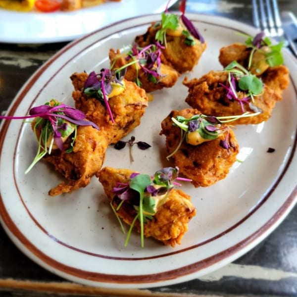 Crispy fried fritters, garnished with microgreens and a creamy sauce, on a white plate.