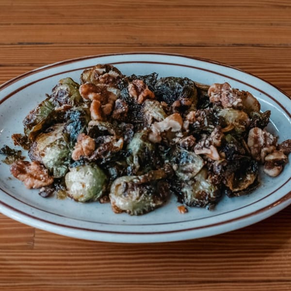 A plate of roasted Brussels sprouts with walnuts on a wooden table at The Wayward Cafe.
