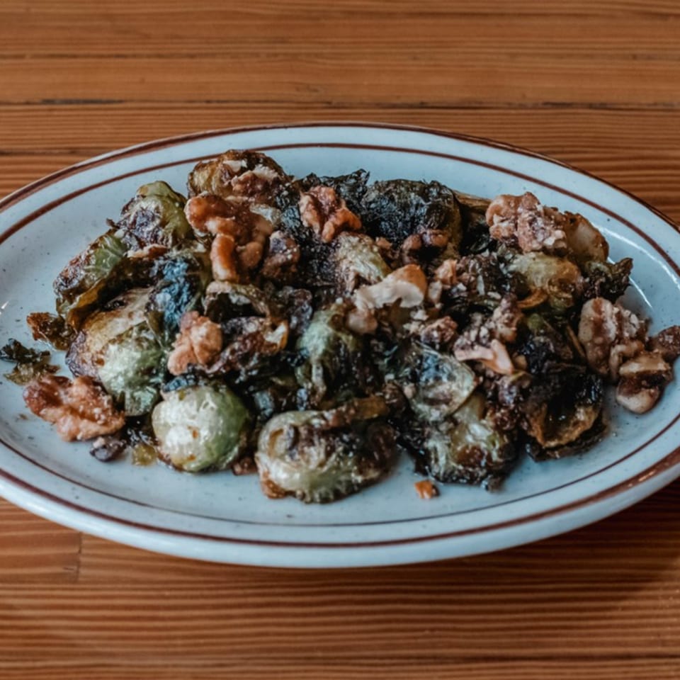 A plate of roasted Brussels sprouts with walnuts on a wooden table at The Wayward Cafe.