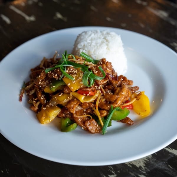 A plate of Wayward Cafe's sweet and sour chicken with bell peppers, onions, and white rice.