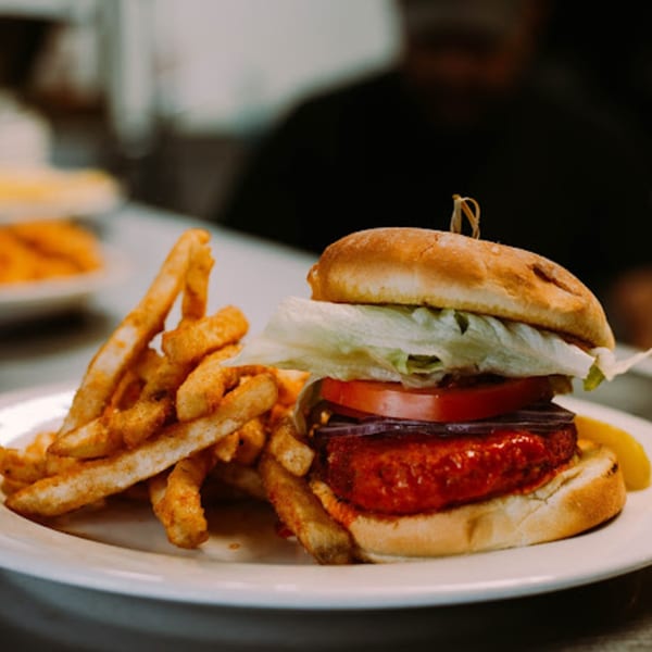 A Wayward Cafe burger with a thick patty, lettuce, tomato, onion, and a side of fries.