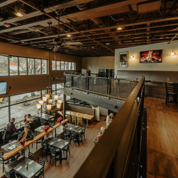 The Wayward Cafe's two-story interior with customers, tables, and large windows overlooking a street.