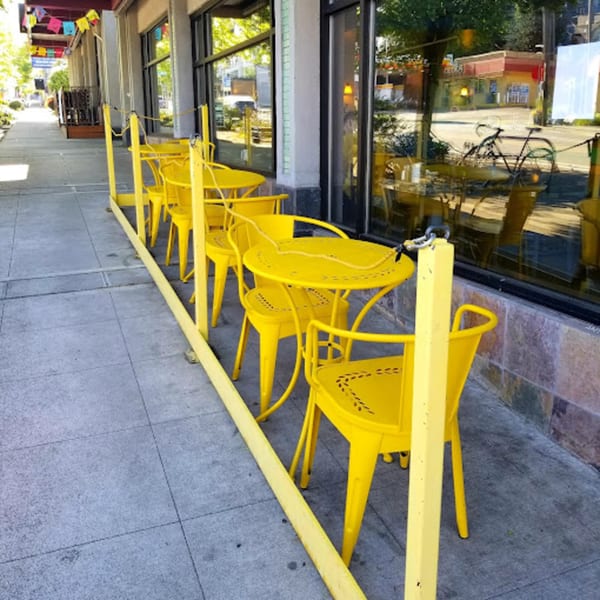 Bright yellow outdoor tables and chairs line the sidewalk outside The Wayward Cafe.